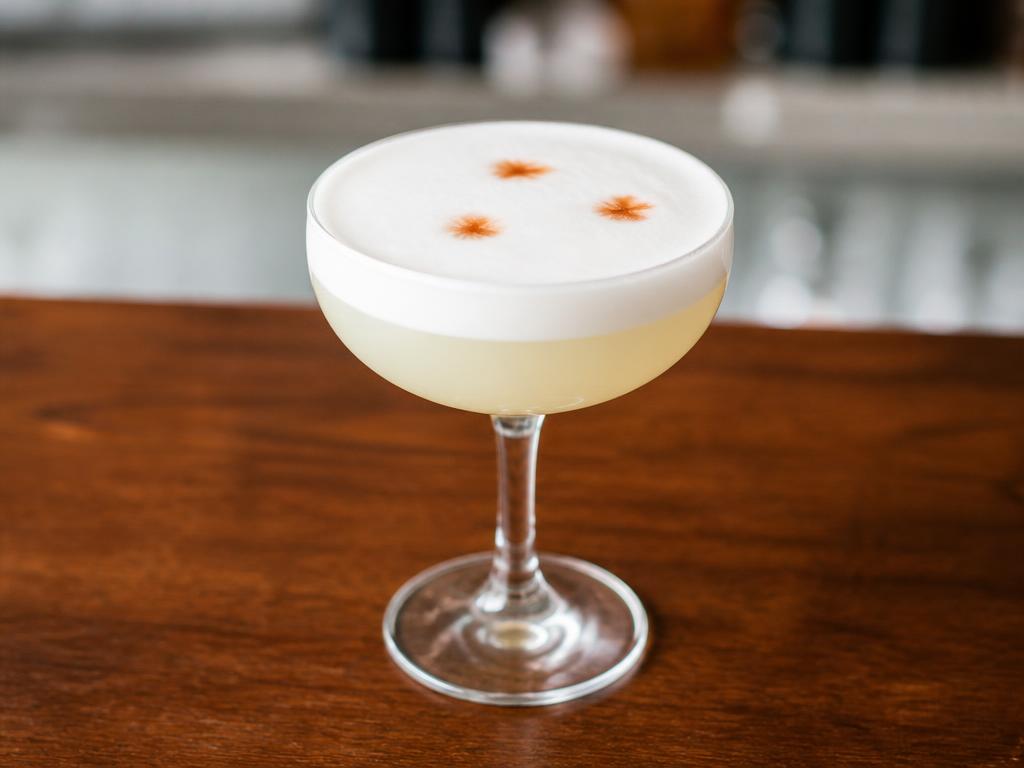Vaaleankeltainen cocktail coupe-lasissa paksun valkoisen vaahdon ja tummien bitterspisaroiden kanssa