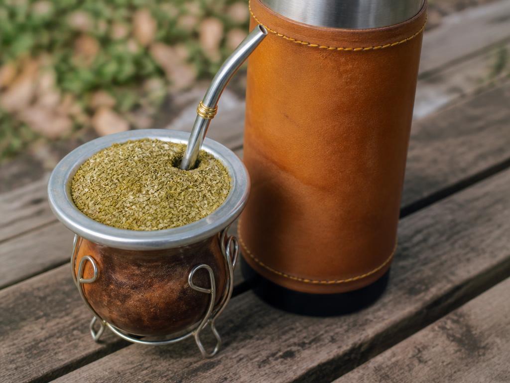 Kurpitsakuppi yerba mate -lehtineen ja metalliputkineen termospullon vieressä